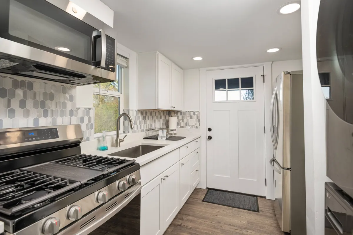 A modern kitchen scene featuring stainless steel appliances, a bright hexagonal backsplash, and crisp white cabinetry. The space exudes a cozy, contemporary vibe, ideal for cooking and entertaining guests.