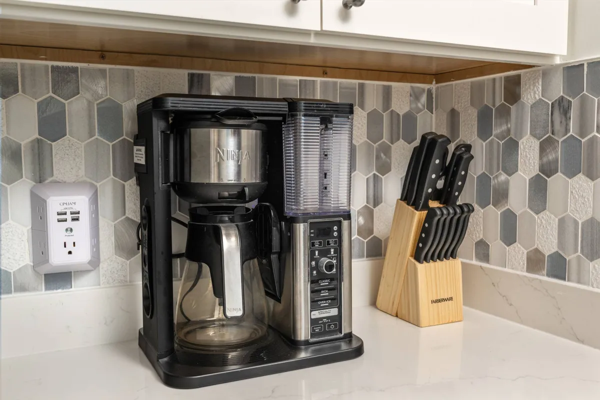 This cozy interior shot showcases a modern kitchen corner, featuring a coffee maker, knife set, and stylish hexagonal backsplash. The setup suggests inviting mornings brewing coffee together and preparing meals, evoking warmth and togetherness. The design balances comfort with a contemporary feel, reinforcing the upgraded, serene environment.