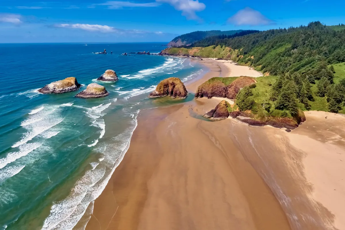 Showcasing a serene beachfront with rocky outcrops, sandy shore, and rolling green hills, this image exudes a relaxed, inviting atmosphere. The waves, beachcombing opportunities, and sunrise-lit waters highlight the outdoor lifestyle accessible from the property.