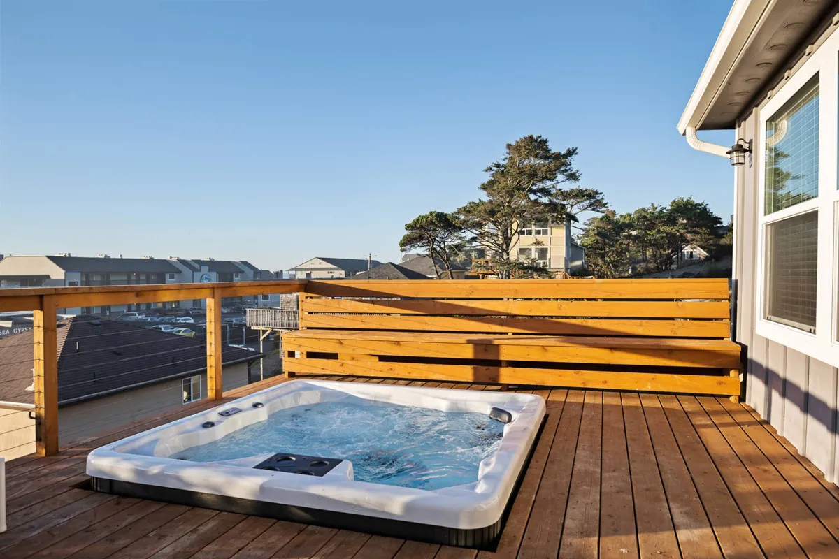 This exterior image captures a tranquil wooden deck nestled among trees, with a sunken hot tub as the focal point. The surrounding natural scenery and open sky create a serene backdrop, perfect for relaxation or stargazing. The deck is inviting for morning coffee or evening unwinding, with privacy and lush greenery enhancing the romantic ambiance.