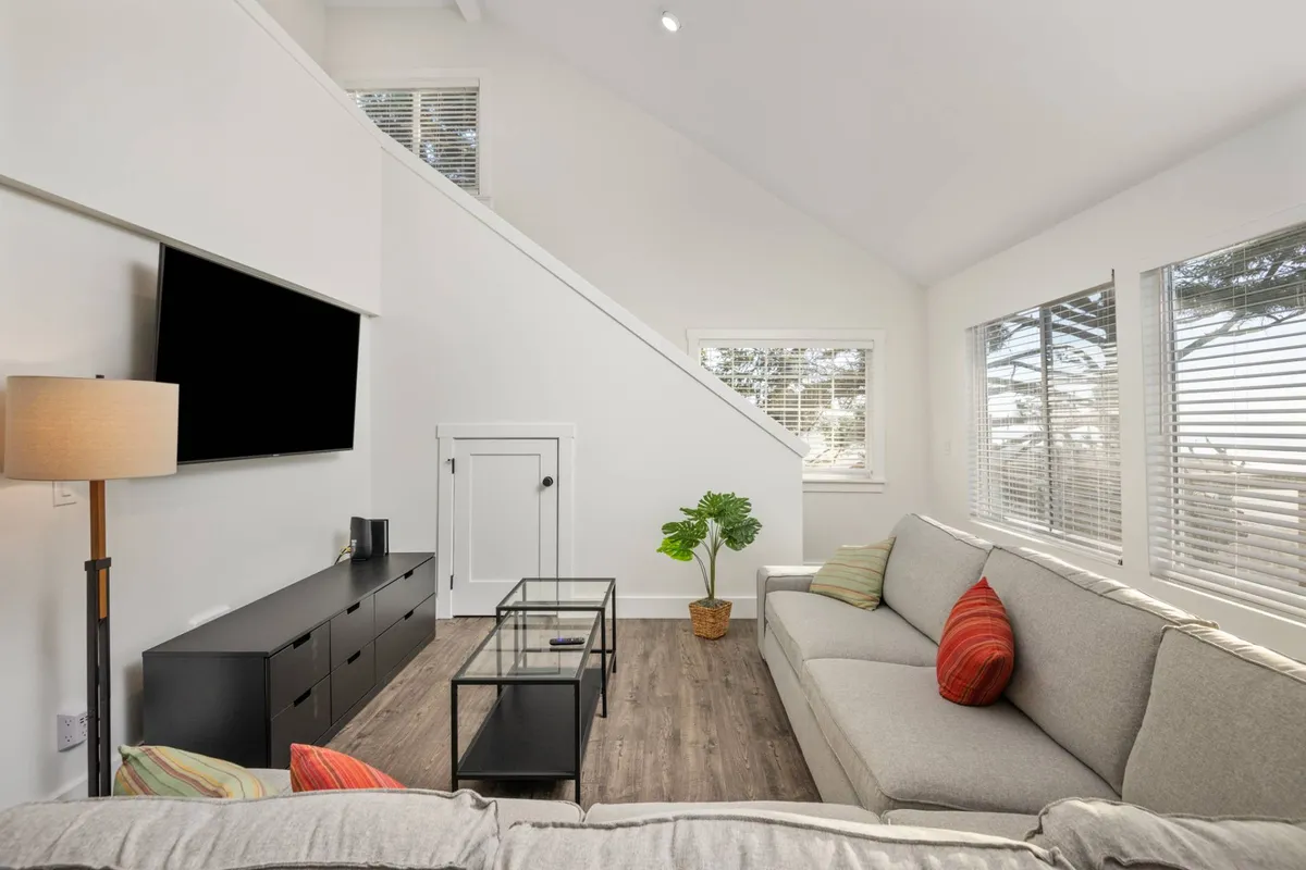 A comfortable living area featuring a sofa with colorful cushions, a glass coffee table, a modern TV stand, and an indoor plant. Sunlight pours in, creating a bright, welcoming space perfect for relaxing, socializing, or movie nights.