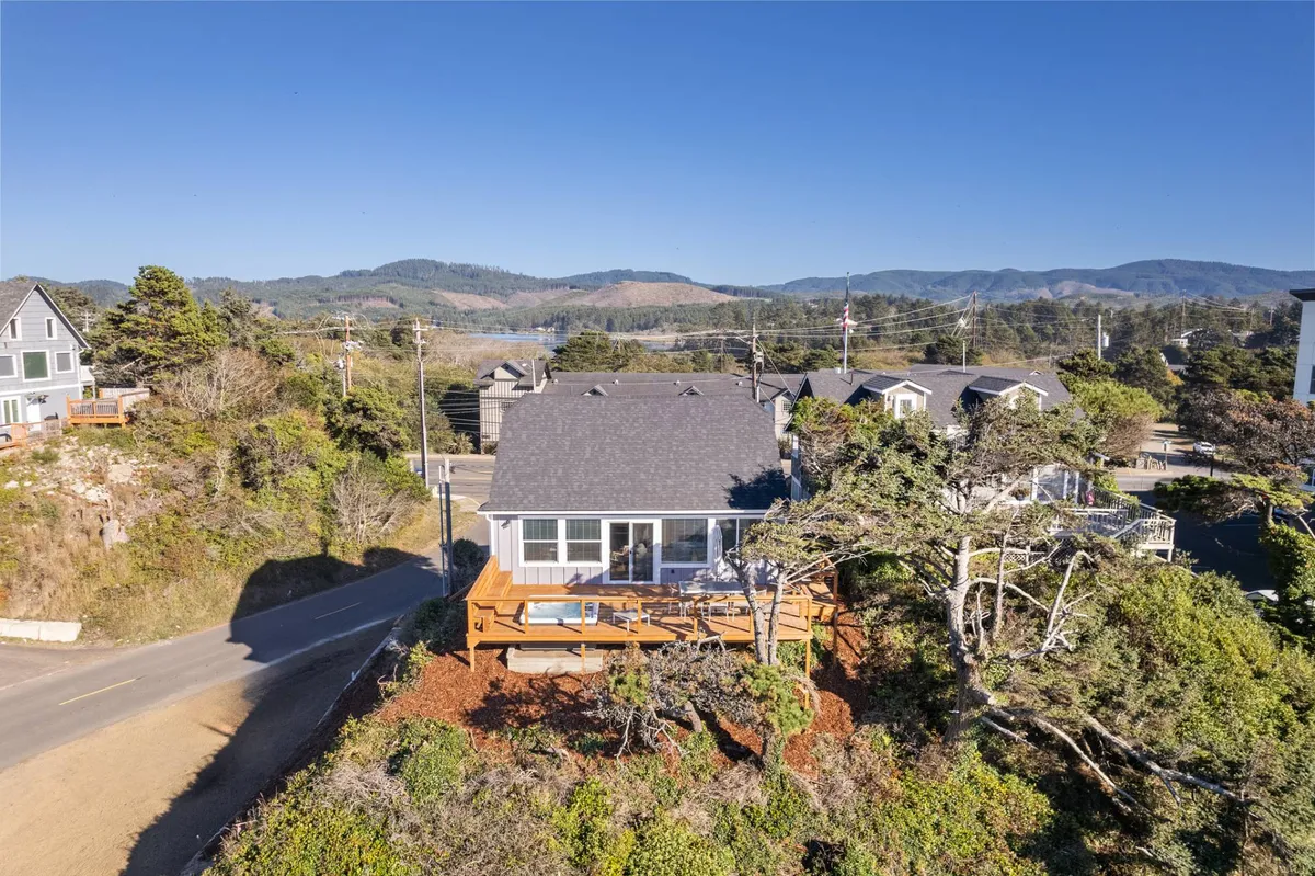 This exterior image showcases the house with a spacious deck surrounded by trees and distant mountains, creating a relaxed and peaceful vibe ideal for guests and their pets to enjoy outdoor time together. The inviting deck is perfect for lounging in the coastal breeze, while the surrounding nature hints at nearby trails and explorations.